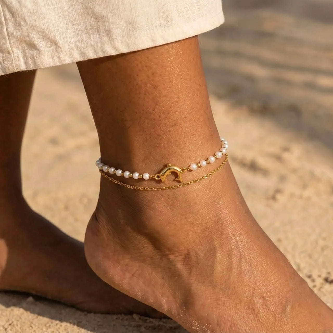 Pearl Dolphin Anklet Set worn on a sunlit ankle, cream freshwater pearls and a polished gold dolphin charm, by Brother & Sisters.