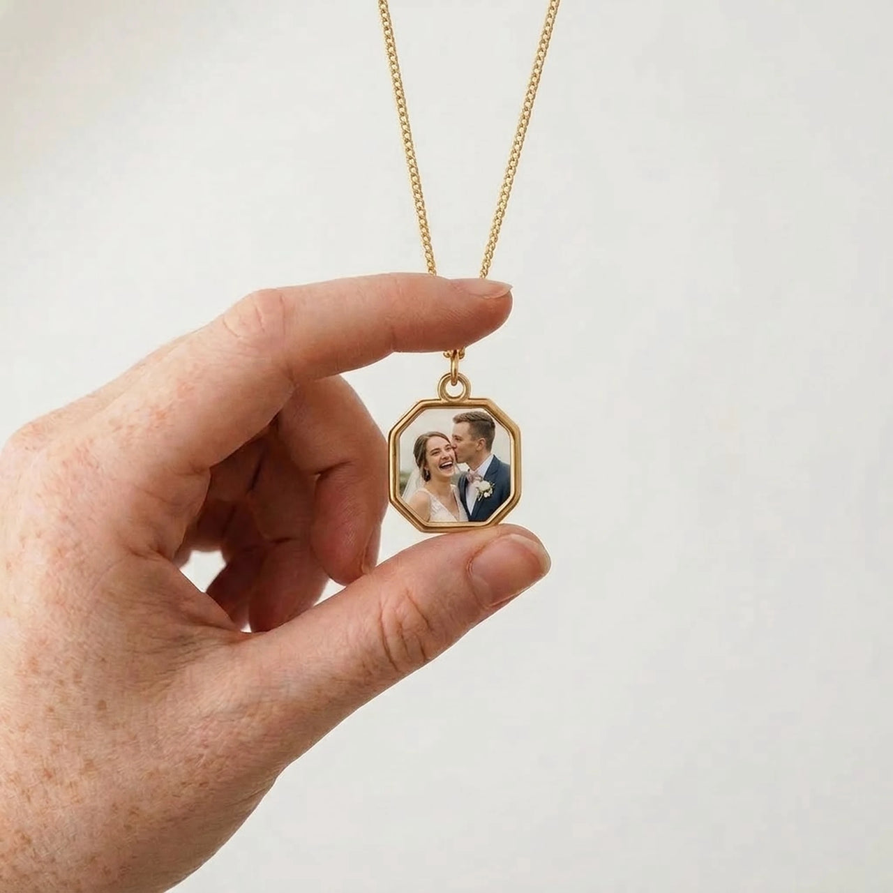 Gold octagon pendant held between two fingers, real small size, wedding photo inside | SKU: TPH-OCTN-GOLD