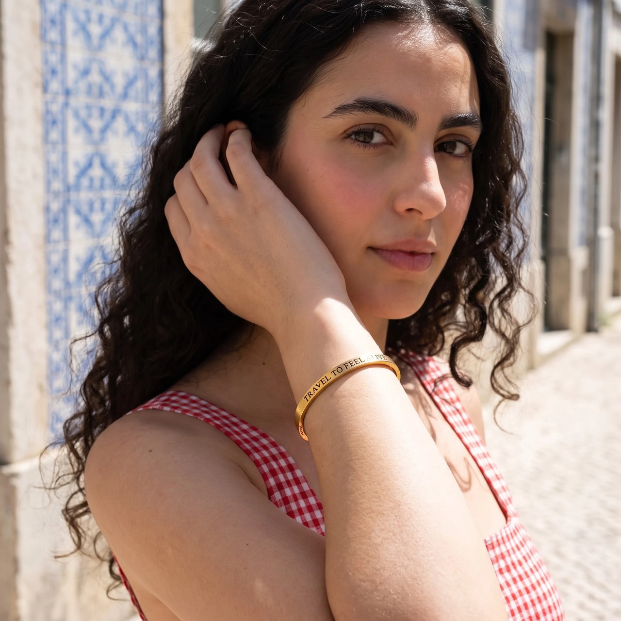 Woman gently touching her Travel To Feel Alive bracelet in gold | SKU: ttfa-g